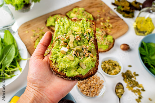 Avocado Guacamole Sandwich in a female hand with pumpkin seeds and wheat seedlings