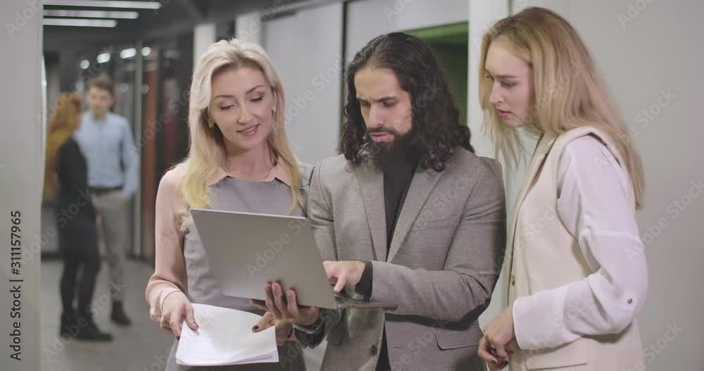 Portrait of two Caucasian women standing on both sides of Middle Eastern man and helping him to deal with laptop. Office workers in open space. Cinema 4k ProRes HQ. Portrait of two Caucasian women standing on both sides of Middle Eastern man and helping him to deal with laptop. Office workers in open space. Cinema 4k ProRes HQ.