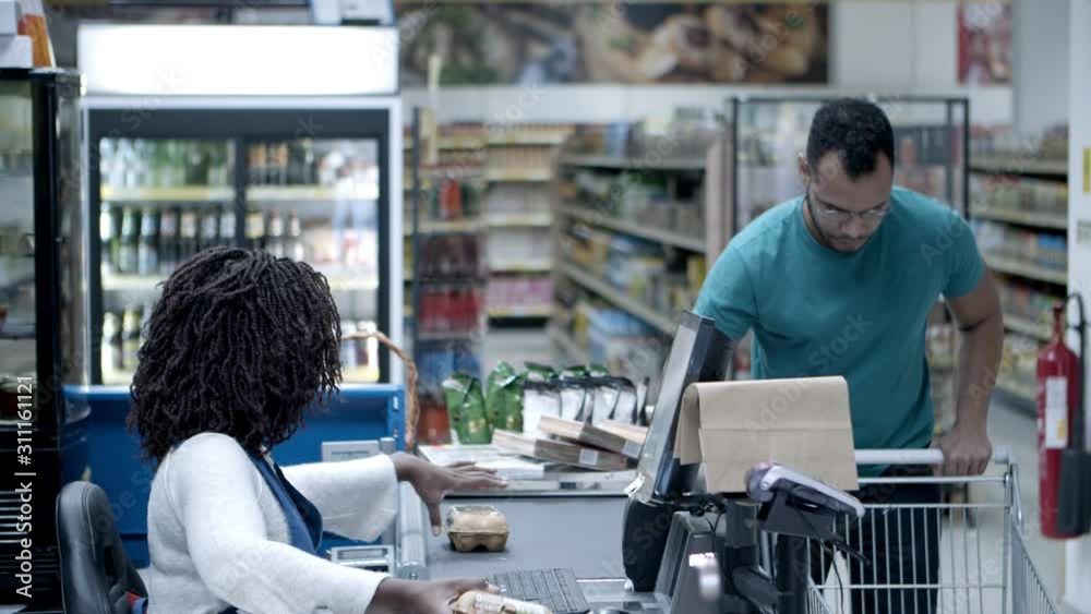 Bearded man buying groceries in supermarket. African American cashier scanning goods at checkout. Shopping concept Bearded man buying groceries in supermarket. African American cashier scanning goods at checkout. Shopping concept