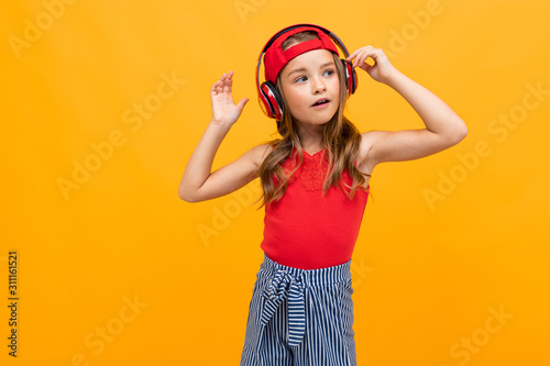 portrait of a cute charming young girl in a casual look with red headphones on a yellow background