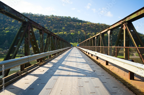 Rusty steel bridge across Dniester river in small village and mountains around. Ukraine.