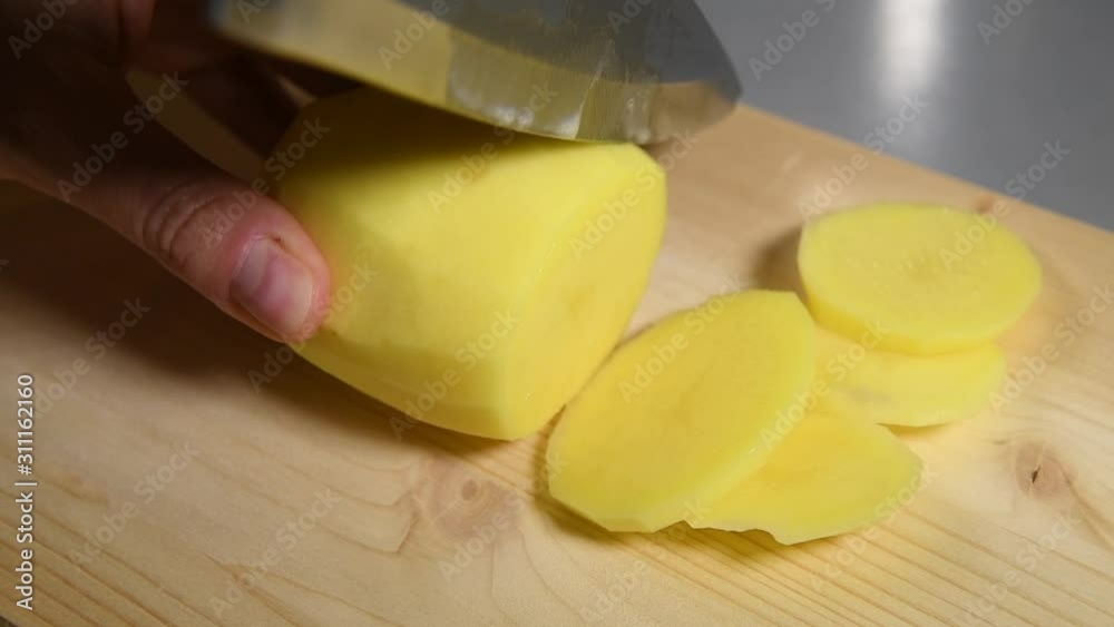 Close up of autentic female hands cutting a potato by knife on cutting board on kitchen table. Cooking potato dishes. Vegetables on cutting board Close up of autentic female hands cutting a potato by knife on cutting board on kitchen table. Cooking potato dishes. Vegetables on cutting board