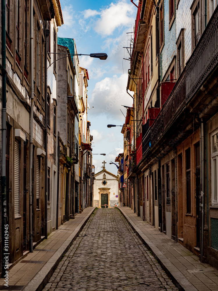 Porto, Portugal. 15 November 2019. Small street lined with colorful town house facades leding uphill towards a small chapel.