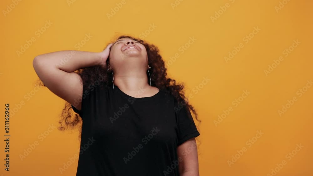 Attractive afro-american overweight woman keeping hand on head, smiling over isolated orange background wearing fashion black shirt. People lifestyle concepte. Attractive afro-american overweight woman keeping hand on head, smiling over isolated orange background wearing fashion black shirt. People lifestyle concepte.