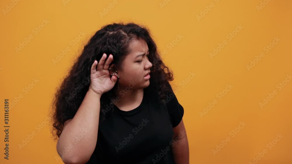 Charming afro-american young lady with overweight over isolated orange background wearing fashion black keeping hand on ear, listening something. People lifestyle concept. Charming afro-american young lady with overweight over isolated orange background wearing fashion black keeping hand on ear, listening something. People lifestyle concept.