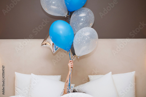 Young woman with balloons lies in bed.