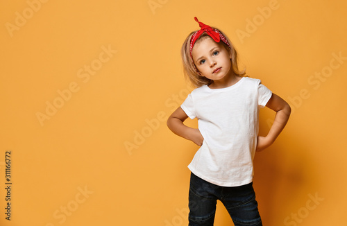 Obraz na płótnie Beautiful little girl in a white T-shirt and a red bandage on her head with blue eyes looks slyly on yellow w salonie