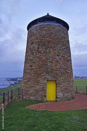 St Monans Windmill in Fife Scotland showing stonework of mill, bright yellow door and gravel curved path with fences to the side. Situated on Fife Coastal Path, Scotland. photo