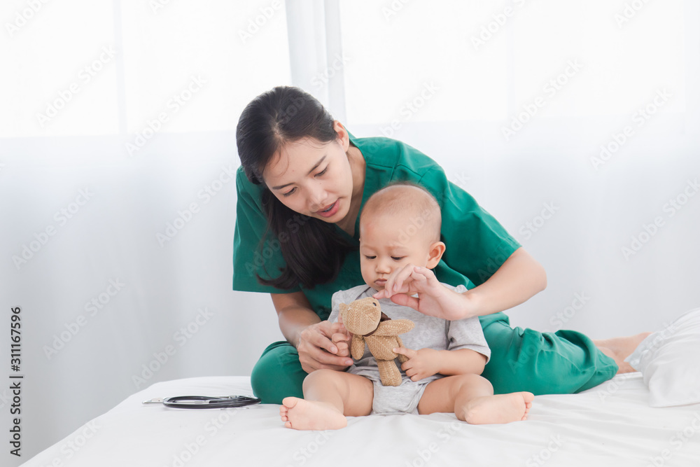 Asian toddler girl get sick examine by pediatrician doctor woman green uniform hold stethoscope, mother or beautiful nurse playing with adorable infant on floor bedroom, child health care concept
