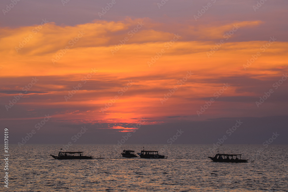 Group of boats on a wide sea during beautiful pink sunset in Cambodia Asia