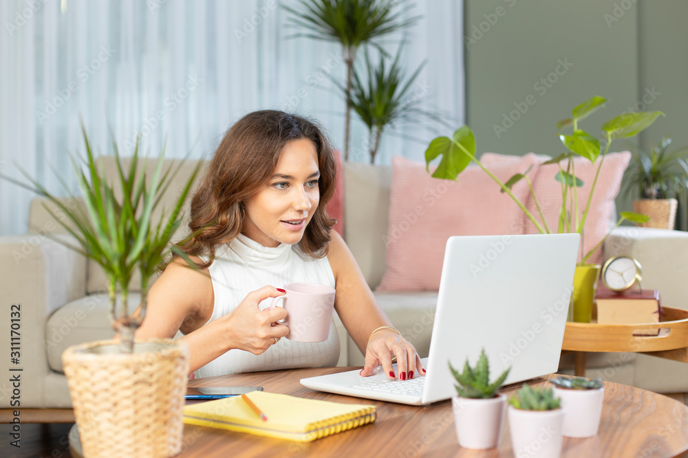 Young woman using laptop while sitting behind table at home Young woman using laptop while sitting behind table at home