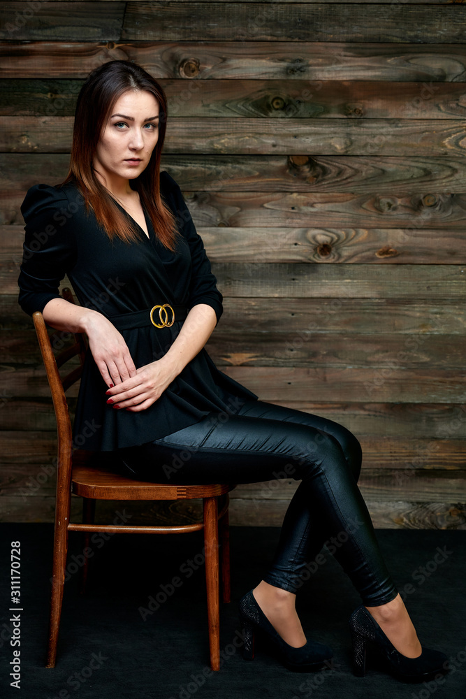 The concept of a glamorous portrait. Portrait of a pretty brunette girl in a black fashion suit on a stylish background in the original interior. Sits on a chair in various poses. The concept of a glamorous portrait. Portrait of a pretty brunette girl in a black fashion suit on a stylish background in the original interior. Sits on a chair in various poses.