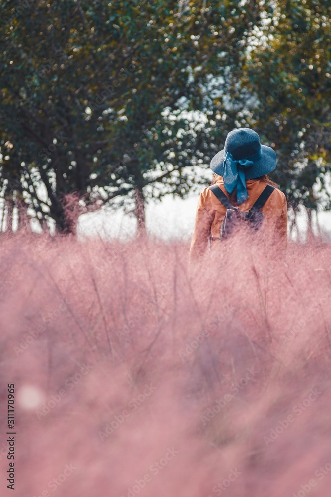 Girl in the blue hat walking through the pink grass field 