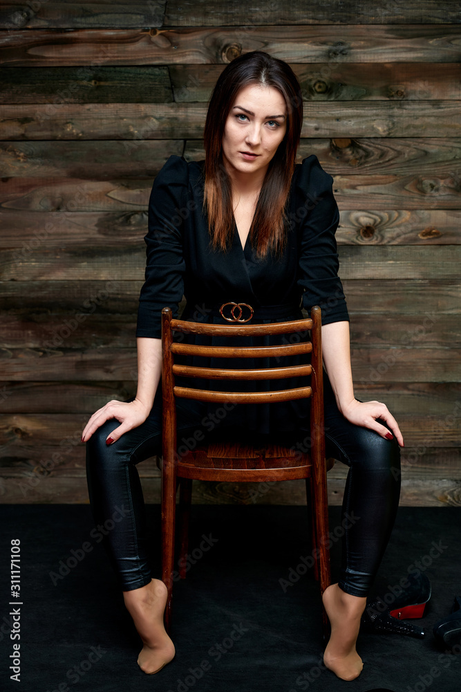 The concept of a glamorous portrait. Portrait of a pretty brunette girl in a black fashion suit on a stylish background in the original interior. Sits on a chair in various poses. The concept of a glamorous portrait. Portrait of a pretty brunette girl in a black fashion suit on a stylish background in the original interior. Sits on a chair in various poses.