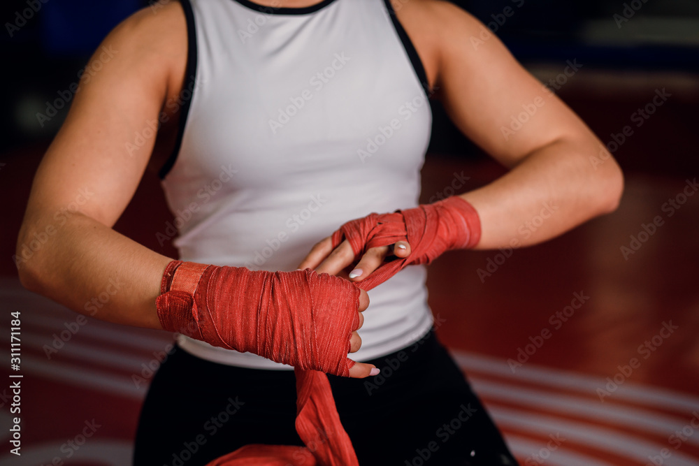 Cropped young muscular woman binds red bandage on hand before training in gym, wearing white sportive top
