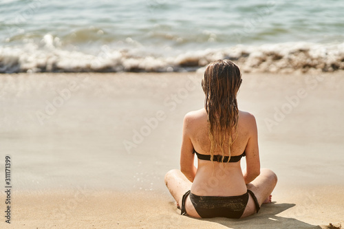 A Young girl is relaxing on the beach. The girl practices yoga