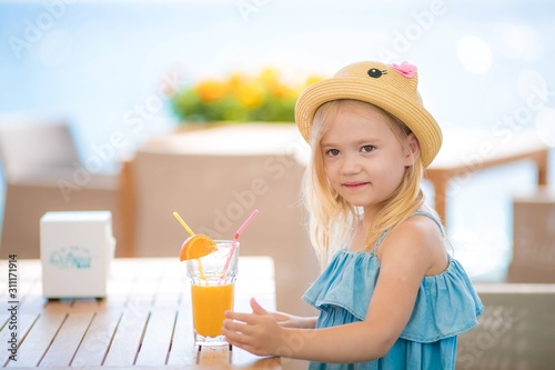 Beautiful blonde girl sitting at the table in the cafe outdoors drinking juice and eating desserts.