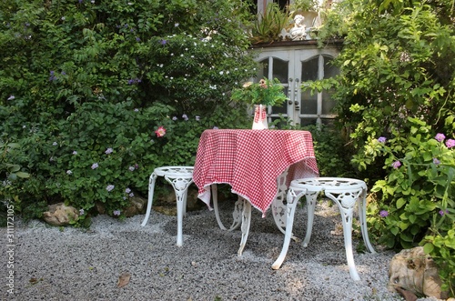 Vintage stools and table with a red checked tablecloth in the corner of an English style garden.