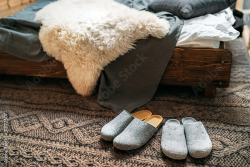 The two pair of gray home slippers near the wooden bed on the 