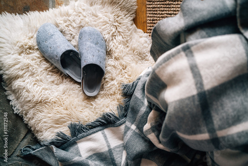 The pair of gray home slippers near the  bed on the white sheepskin in the cozy bedroom. Home sweet home concept top view image. photo