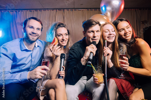 good-looking cheerful happy young people have party time in karaoke bar, wearing party dresses and shirts. Holiday, celebration, party concept