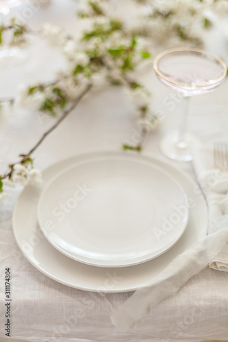 Table setting for a цуввштп dinner with flowering cherry tree branches on the table. Vintage champagne glasses on the white linen tablecloth. 