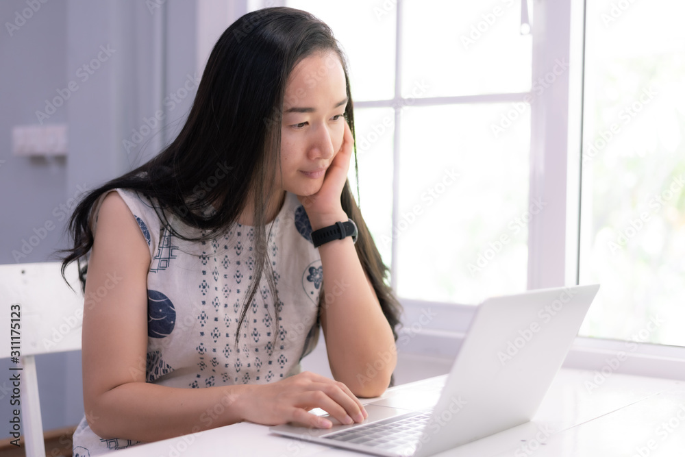 Beautiful asian girl using a notebook or laptop computer at her home and smiling happily. Beautiful asian girl using a notebook or laptop computer at her home and smiling happily.