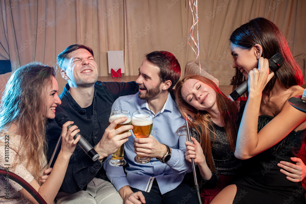 happy cheerful adults, women and men spending day-off in karaoke bar, young ladies and guys wearing party clothes, dresses. energetic and emotional group of people have fun