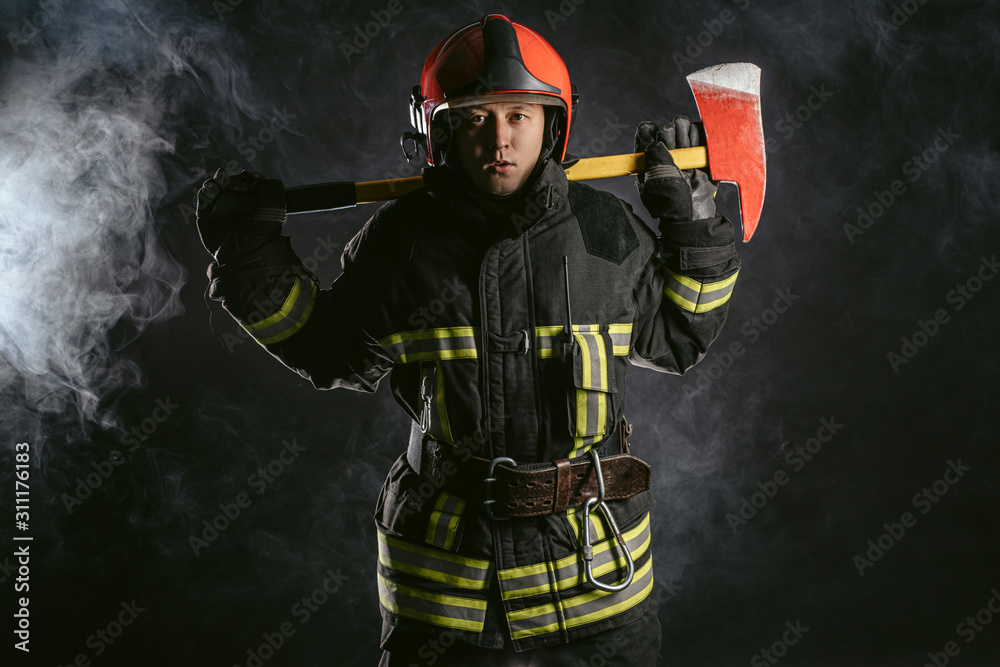 Naklejka premium young adult firefighter saving people from fire wearing uniform and helmet, holding fire fighting equipment