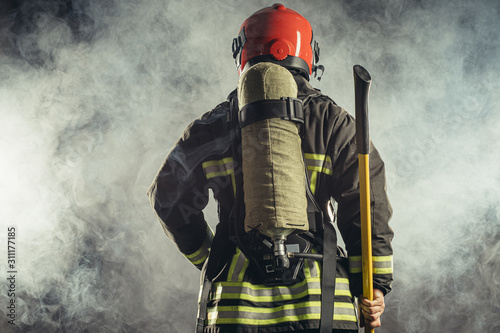rear view on reverent, confident man working in fire station ready to save people from fire in emergency situations, wearing uniform and helmet