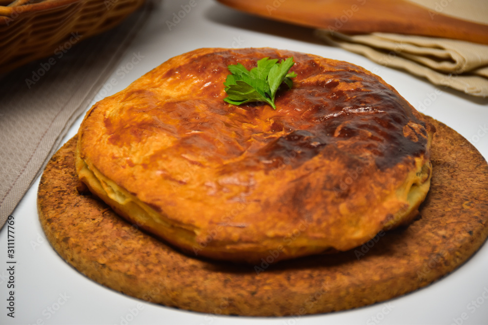 An Australian meat pie on a white background. Wooden spatula in the back. An Australian meat pie on a white background. Wooden spatula in the back.