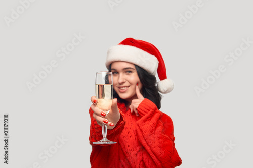 Beautiful brunette girl in a red sweater and Santa hat holding glass of champagne.