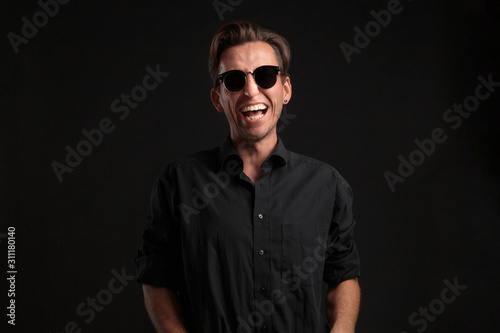 Stylish handsome man a black shirt and sun glasses isolated over black background. Low key portrait
