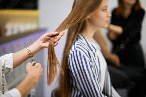 side view on beautiful caucasian girl sitting on chair in beauty salon, closeup of long hair, hairdresser hands holding them, going to cut split ends. Beauty, hair concept © alfa27