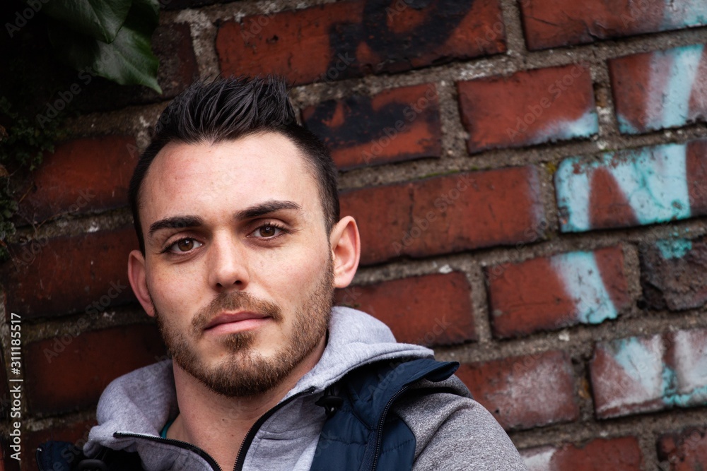young man with modern haircut and hoodie in front of brick wall young man with modern haircut and hoodie in front of brick wall
