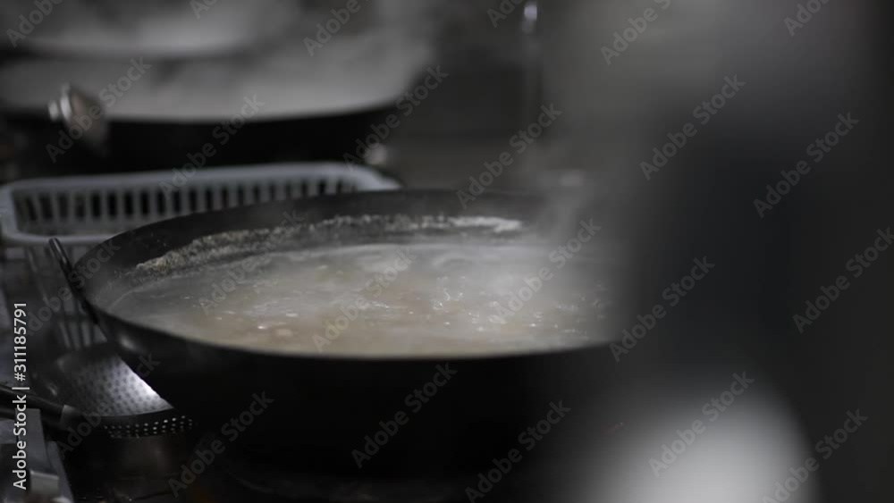 A handheld shot of a man boiling food with a wok in a restaurant. A handheld shot of a man boiling food with a wok in a restaurant.