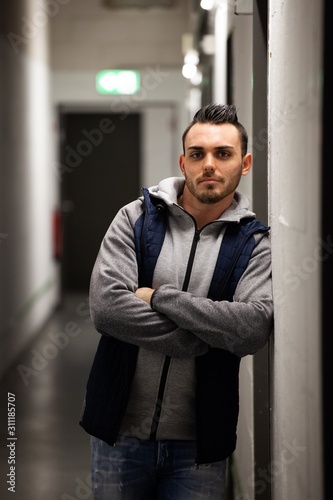 young man with modern haircut wearing hooded sweatshirt in gray hallway