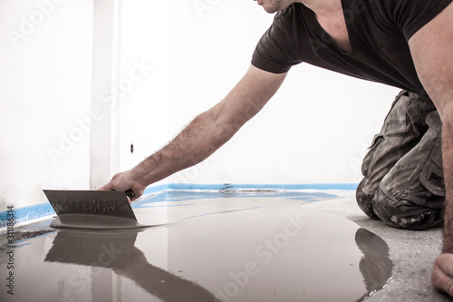 Bauarbeiter rührt Ausgleichsmasse an, spachtelt den Fußboden und bereitet so den Boden für das Parkettlegen vor