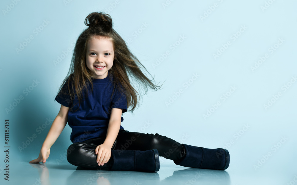 Small smiling girl model with long hair in stylish casual clothing and ugg  boots sitting on floor Stock Photo | Adobe Stock