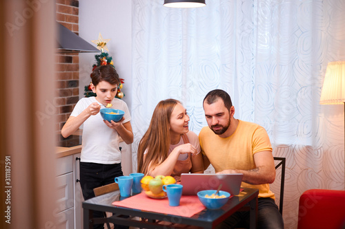 young caucasian married couple, lovely wife and husband sit together at table while their kid boy have meal near them, happy famly concept photo