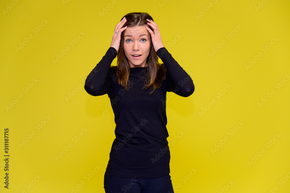 The concept of a smiling cute girl with positive emotions. Portrait of a young woman in a black T-shirt stands in different poses with long hair on a yellow background. Shows hands, talking. The concept of a smiling cute girl with positive emotions. Portrait of a young woman in a black T-shirt stands in different poses with long hair on a yellow background. Shows hands, talking.