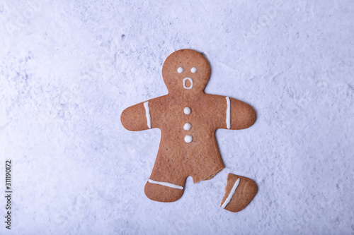 Gingerbread man with a broken leg (without leg) and with a surprised face. Traditional New Year and Christmas homemade cookies. Selective focus, close up.
