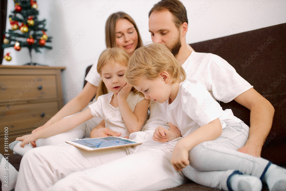 young beautiful family spend time together at home using modern gadgets, tablet. happy family sit on sofa in casual white clothes at home