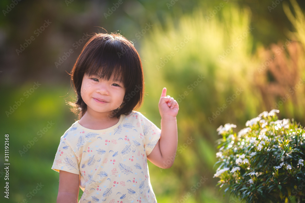 Sweet Asian little child stands to watch the flowers in a green meadow reflect the golden yellow sun. Bright spring with a cute young girl. Baby age 2 years 9 months old. Sweet Asian little child stands to watch the flowers in a green meadow reflect the golden yellow sun. Bright spring with a cute young girl. Baby age 2 years 9 months old.
