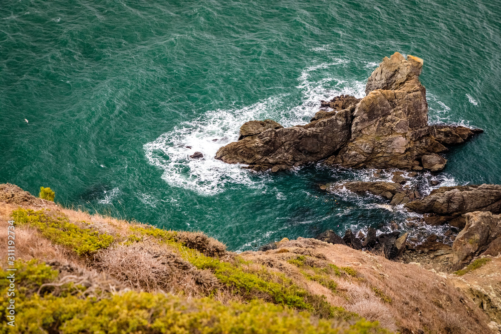 Looking down onto a rocky outcropping with frothy white waves around the shore