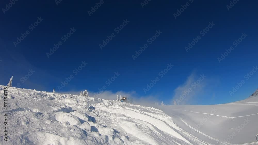 a Pro snowmobiler makes a jump with a big blast of snow and epic falls. background of mountain valley, leaving behind a trail of splashes. bright snow bike and suit. snowmobile a Pro snowmobiler makes a jump with a big blast of snow and epic falls. background of mountain valley, leaving behind a trail of splashes. bright snow bike and suit. snowmobile
