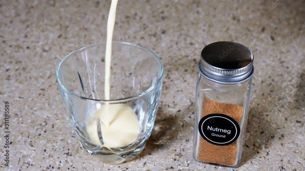 Close-up shot of a person pouring eggnog into a clear glass and sprinkling nutmeg on top Close-up shot of a person pouring eggnog into a clear glass and sprinkling nutmeg on top