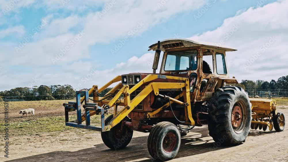 A rusty old tractor moves slowly over an Australian farm towing a seeder. Tracking shot A rusty old tractor moves slowly over an Australian farm towing a seeder. Tracking shot