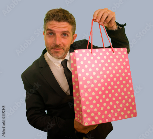 isolated background portrait of young attractive and happy business man in suit and tie holding shopping bag smiling cheerful in sales and opportunity concept and consumerism