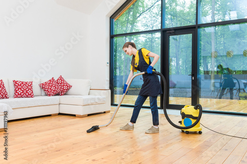 professional cleaning service. woman in uniform and gloves does the cleaning in a cottage. the worker vacuums the floor with professional equipment